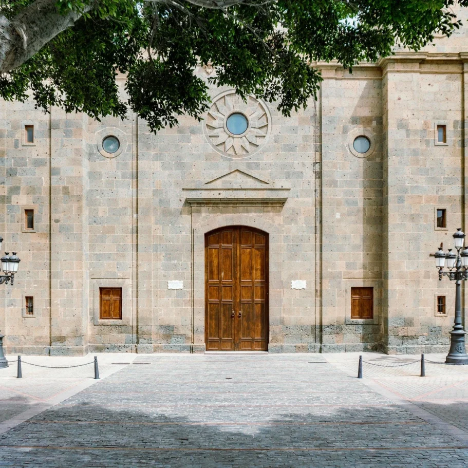 städtische & öffentliche Einrichtungen Fassade einer historischen Steinkirche mit großen Holztüren und runden Fenstern.