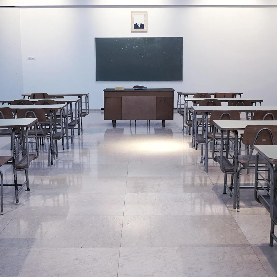 Schulen & Kindergärten Leeres Klassenzimmer mit Tischen, Stühlen und einer Tafel an der Wand.