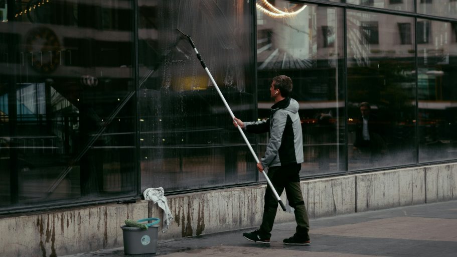 Fensterreinigung Ein Mensch reinigt mit einem langen Stab ein Schaufenster in einer urbanen Umgebung.